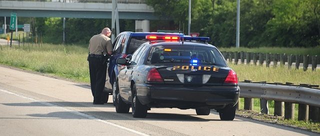Traffic Ticket Police Vehicle - A police cruiser with the lights flashing has stopped a speeding car along the interstate highway and is issuing a ticket.